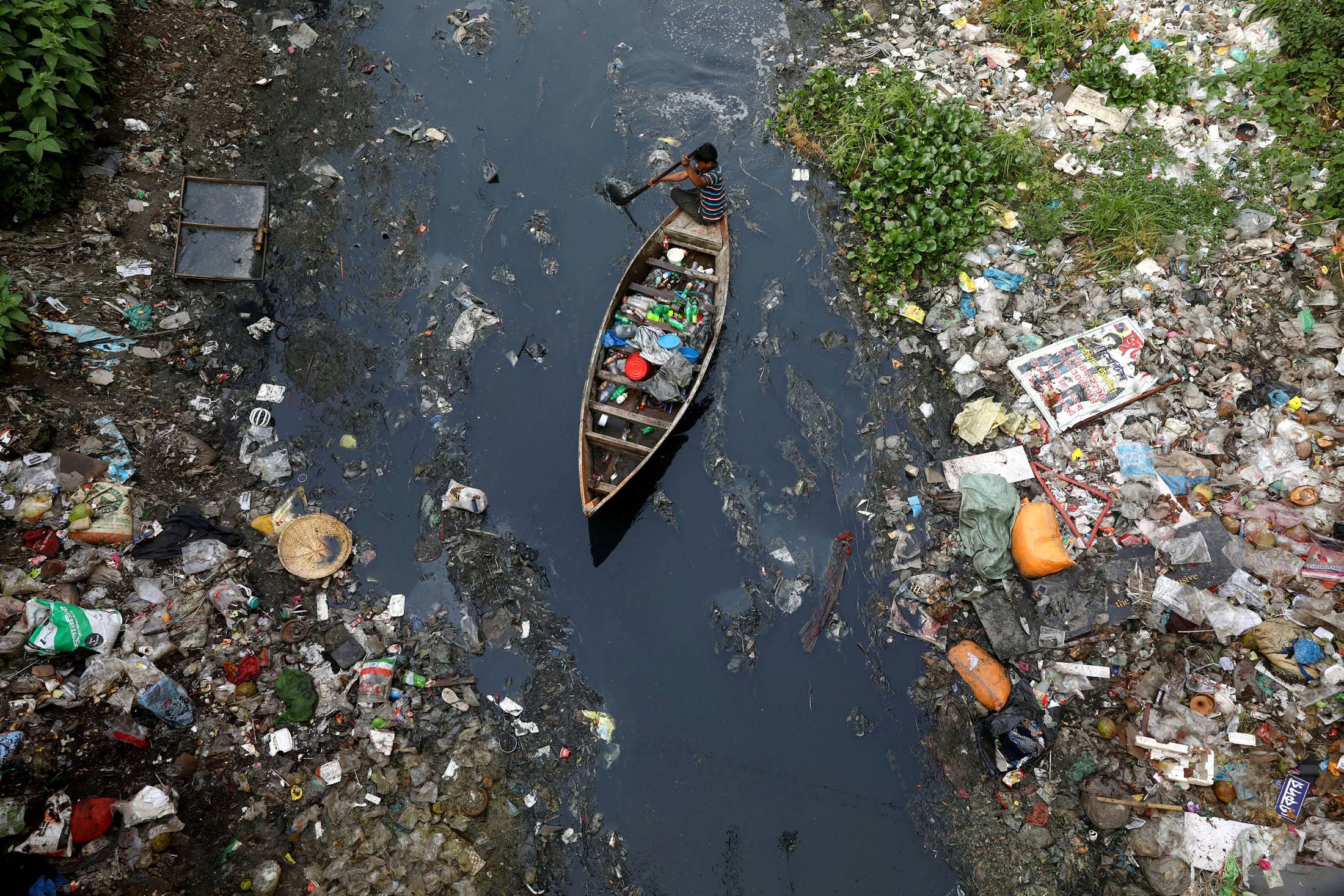 A boy collects plastic from a stream in Dhaka, Bangladesh